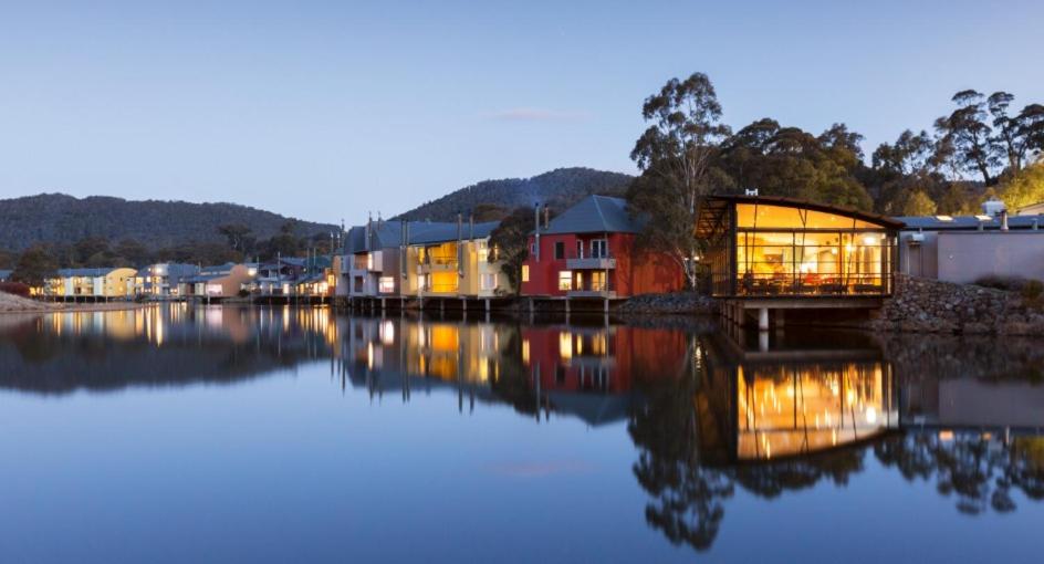 Lake Crackenback Resort — timber-and-glass chalet reflected in a still alpine lake ringed with snow-dusted mountains.