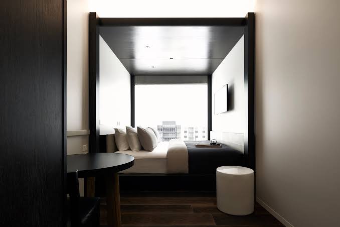 Little National Hotel Canberra — refined compact suite with lake-facing glass, walnut joinery and a floating bed platform.