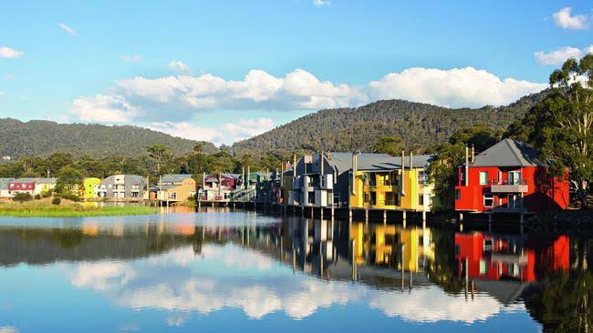 Novotel Lake Crackenback — colourful lakeside chalets on stilts reflected in calm alpine water at dusk.