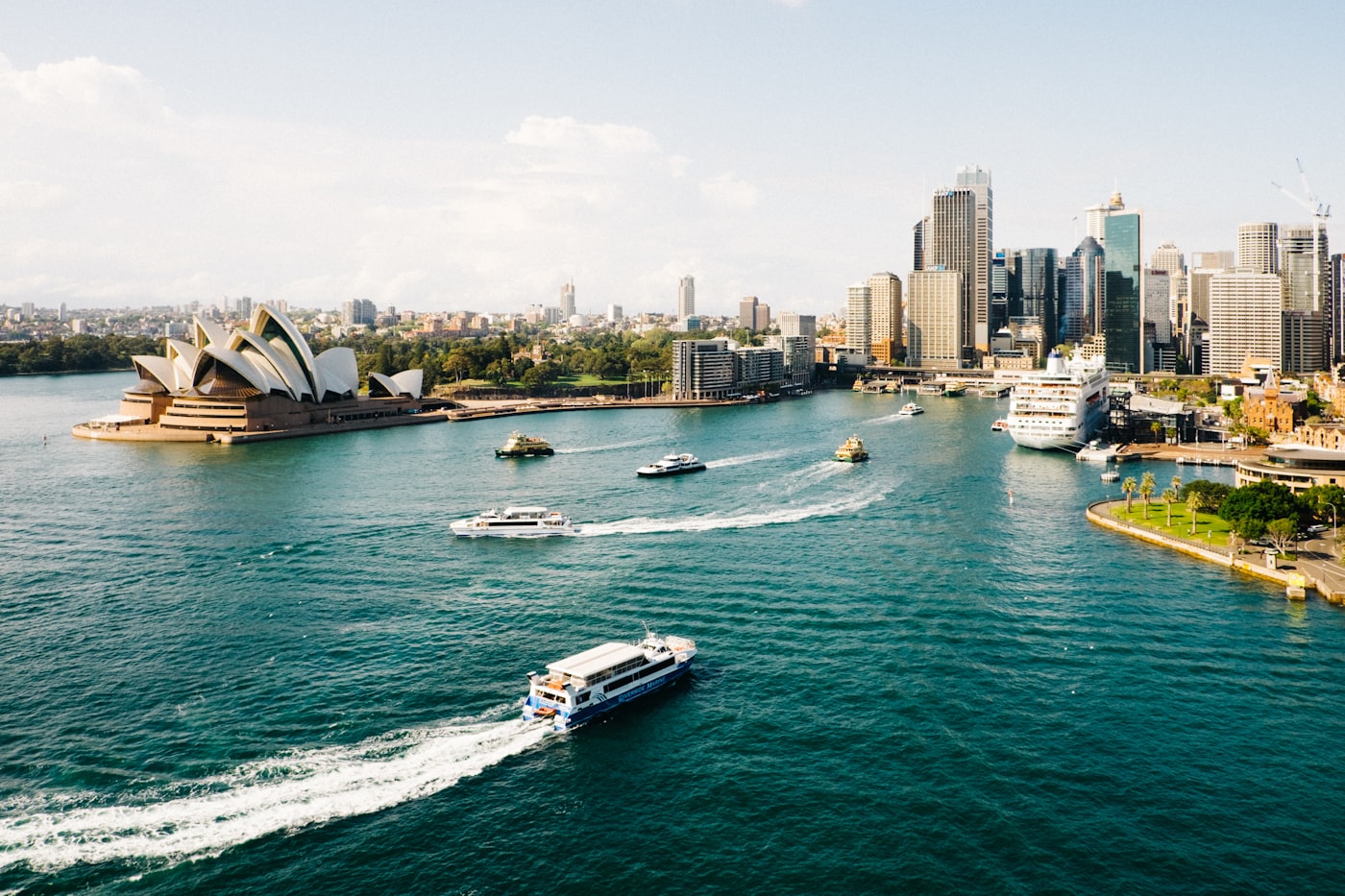 Editorial photograph: a warm-lit boutique suite above Sydney Harbour at first light, linen drapes, brass fittings, the Opera House sails soft in the distance.