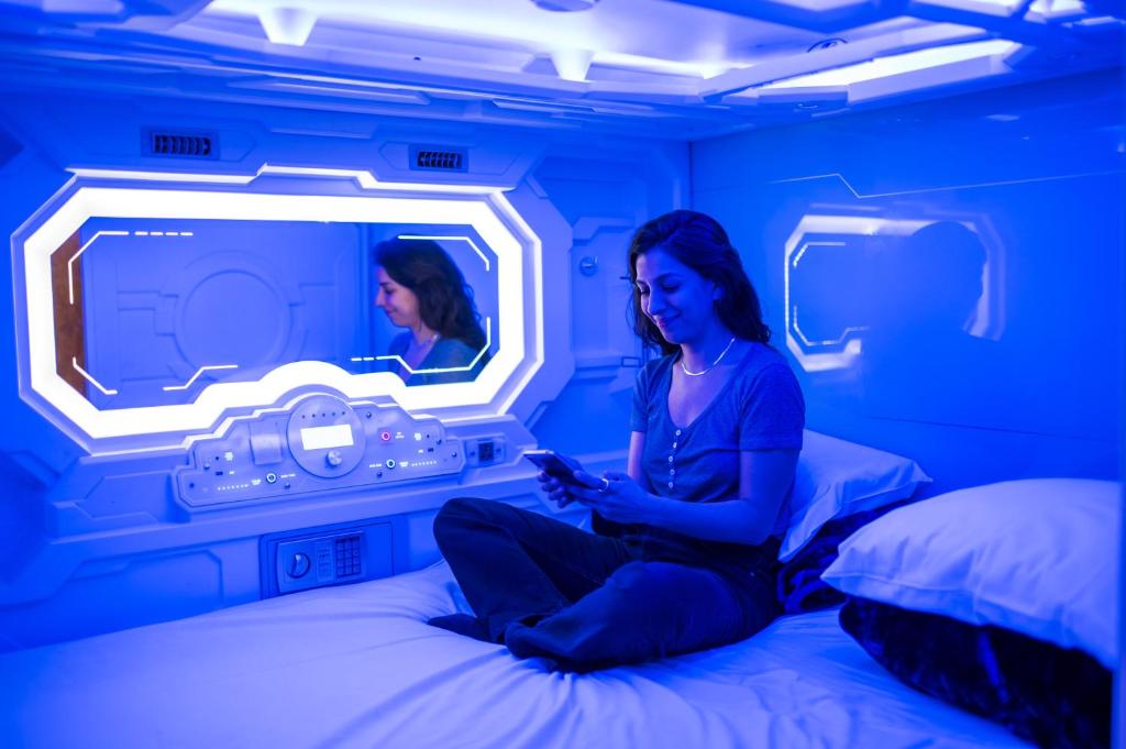 Space Q Capsule Hotel, Sydney — glowing individual sleep capsules in a warm-lit dormitory pod bay, clean and futuristic.